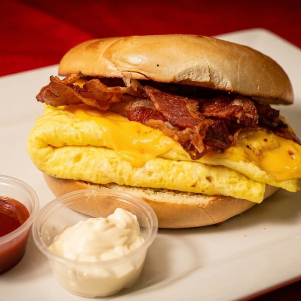 Breakfast sandwich with scrambled eggs, cheese, and bacon on a bagel, with ketchup and mayonnaise.
