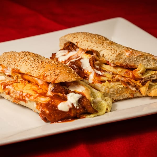 Two loaded subs with red sauce, white sauce, and cheese on a white plate.
