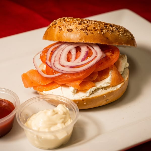Sesame bagel with cream cheese, smoked salmon, tomato, and red onion, with two dipping sauces.