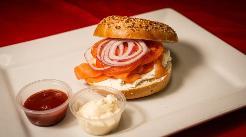 Sesame bagel with cream cheese, smoked salmon, tomato, and red onion, with two dipping sauces.